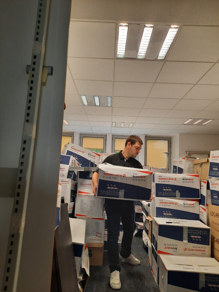 Salarié pendant le déménagement, au milieu de nombreux cartons de déménagement dans un bureau, transportant un carton.