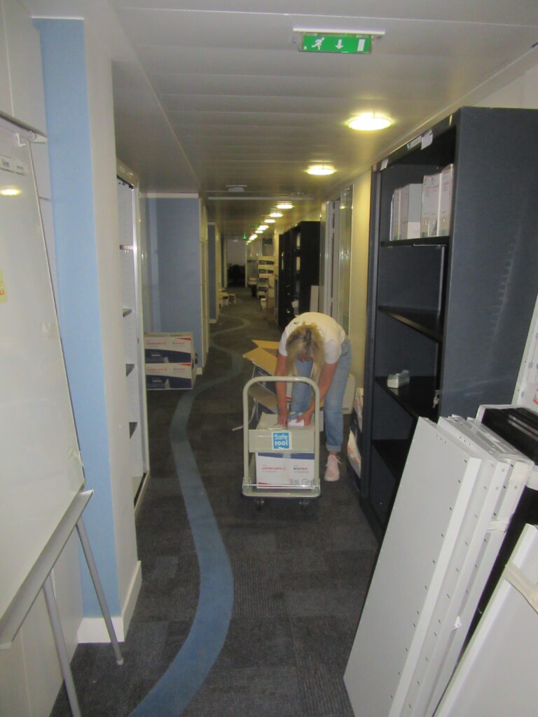 Salariée pendant le déménagement, rangeant des boîtes dans armoires avec l'aide d'un charriot dans le couloir.
