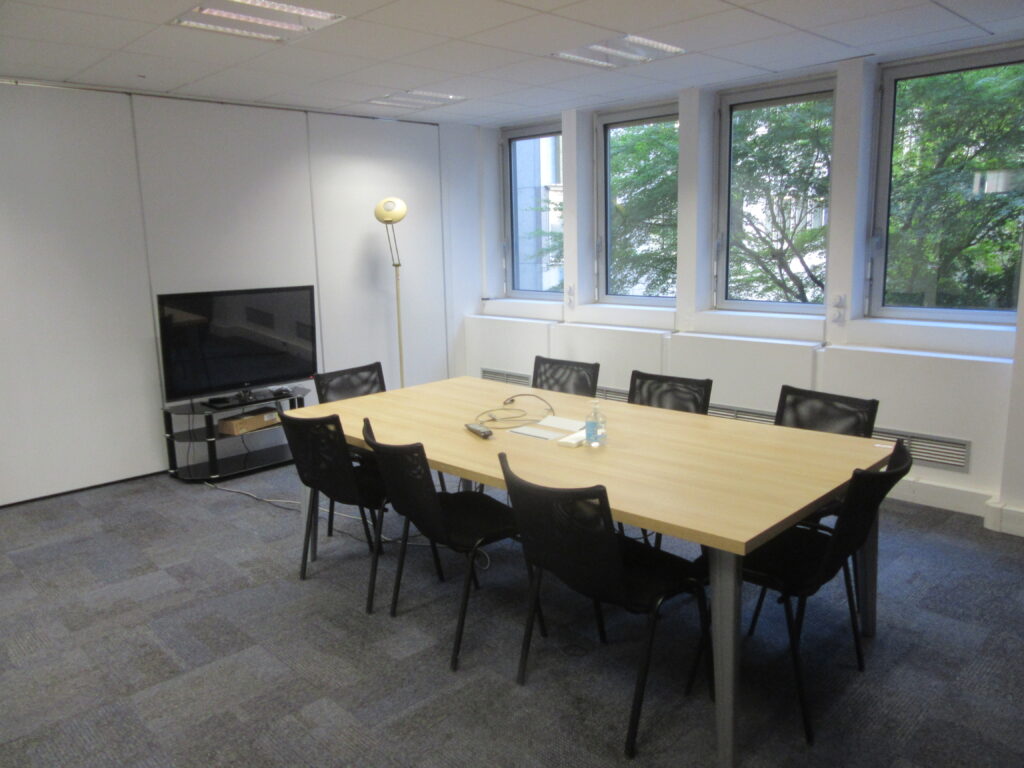 Salle de réunion avec une table, des chaises, des fenêtres et un écran.